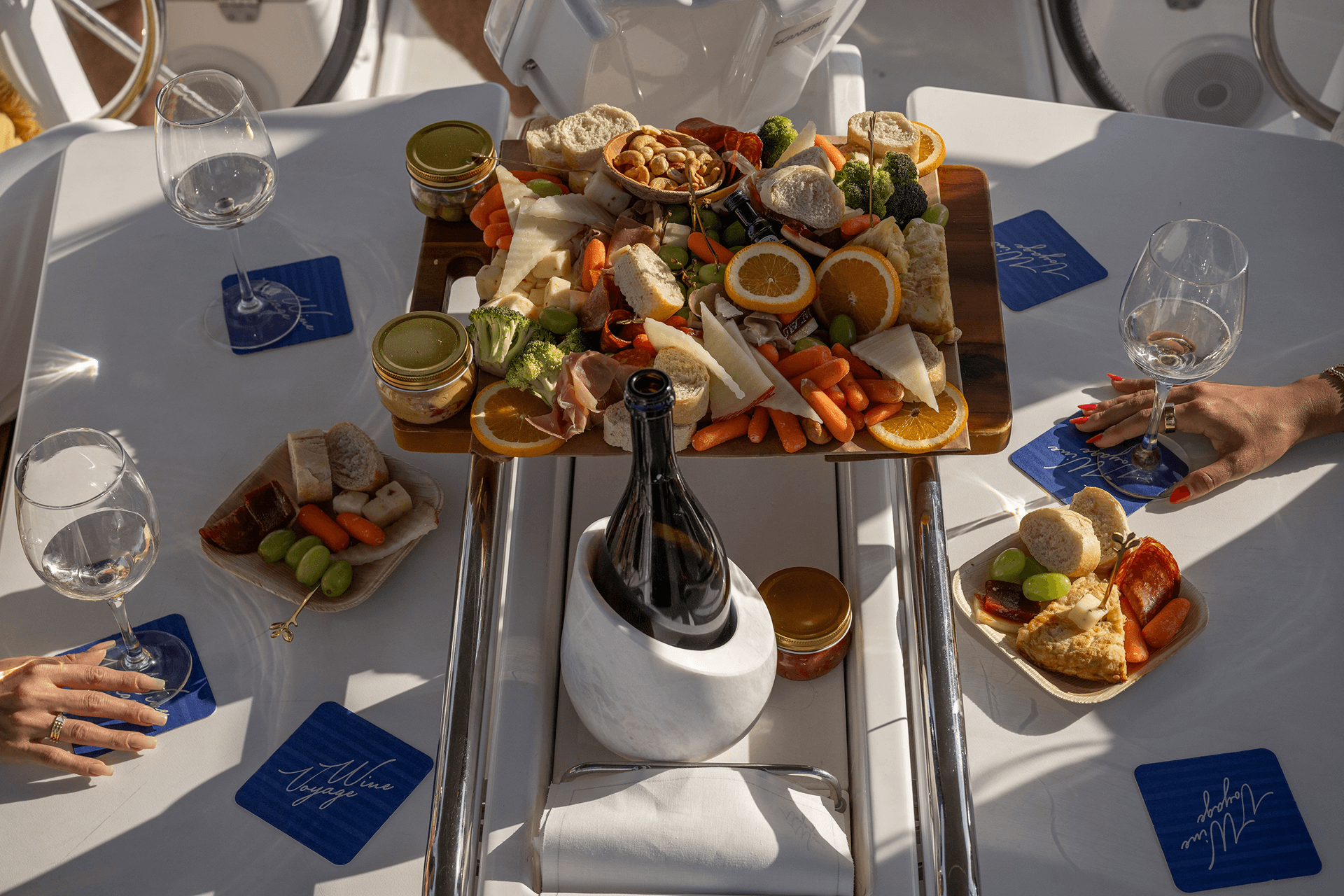 A cheese and charcuterie board laid out on deck with wine glasses and champagne