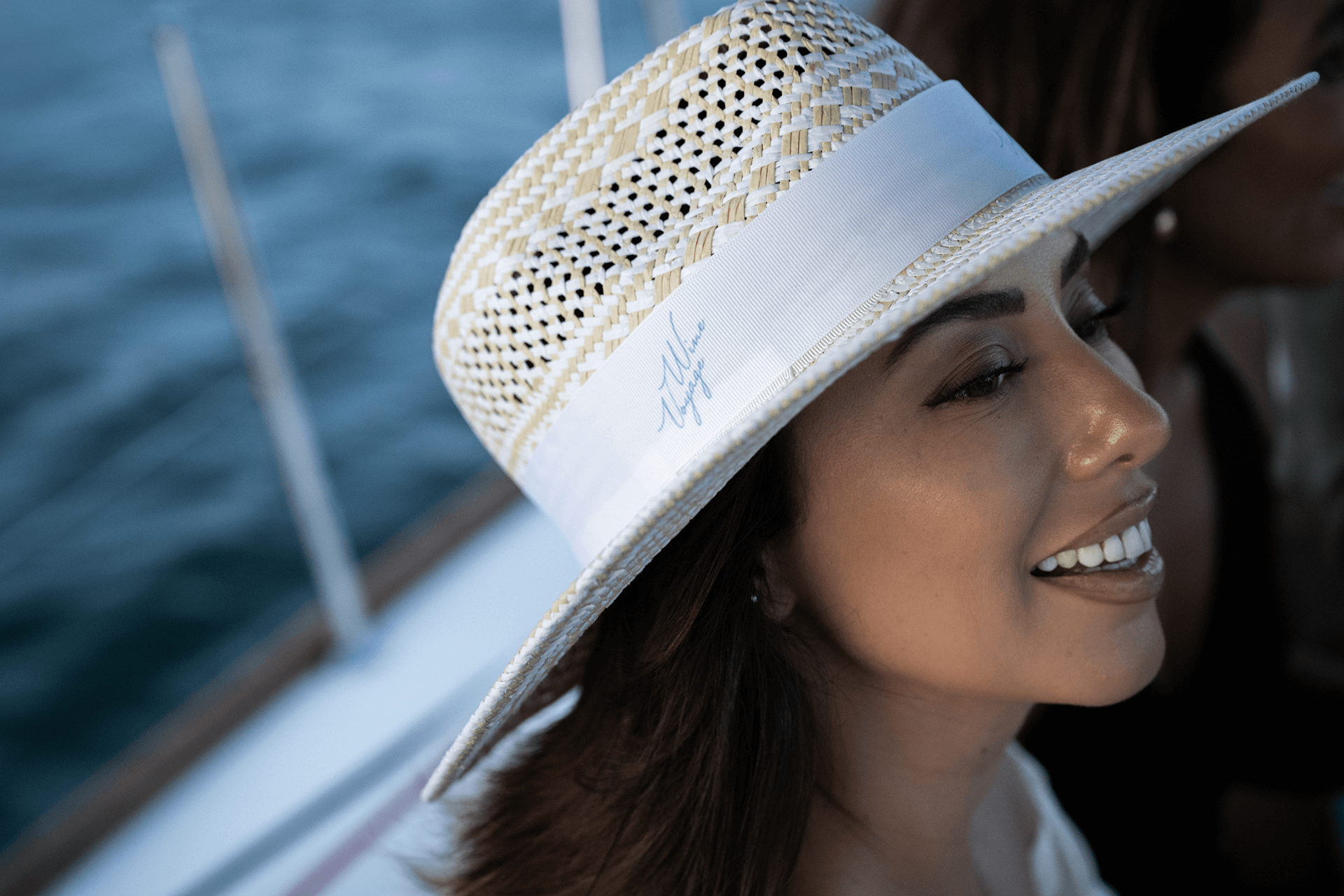 A guest in a sun hat smiling beside the mainsail